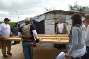 "Volunteers participating in dayitwa NGO activities, working together to carry wooden frames during a community building project in front of a rustic shelter."